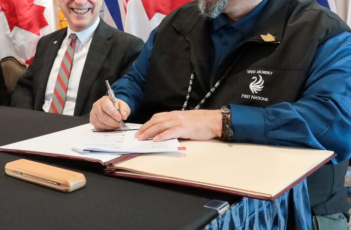 A photo of a First Nations man signing a document